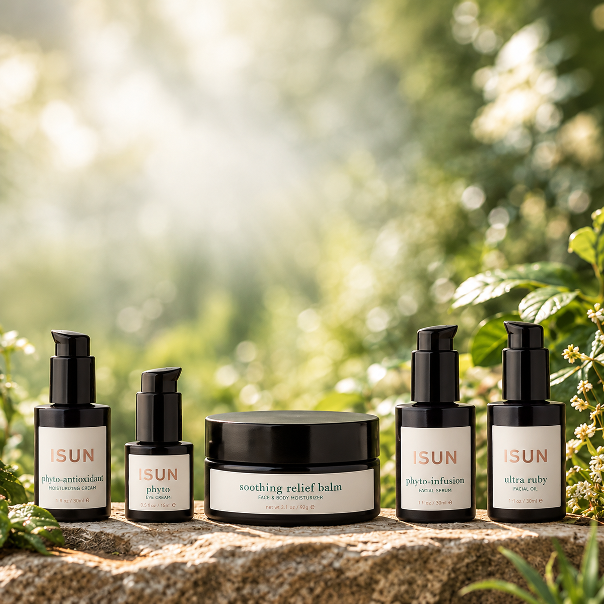 Five ISUN skincare products arranged on a stone surface outdoors with a soft green bokeh background. The products include photo-antioxidant, phyto, soothing relief balm, photo-infusion, and ultra-ruby ampoules and jars with black packaging and white labels.