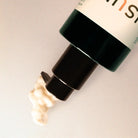 Cosmetic bottle with black cap and visible brand name on a light background