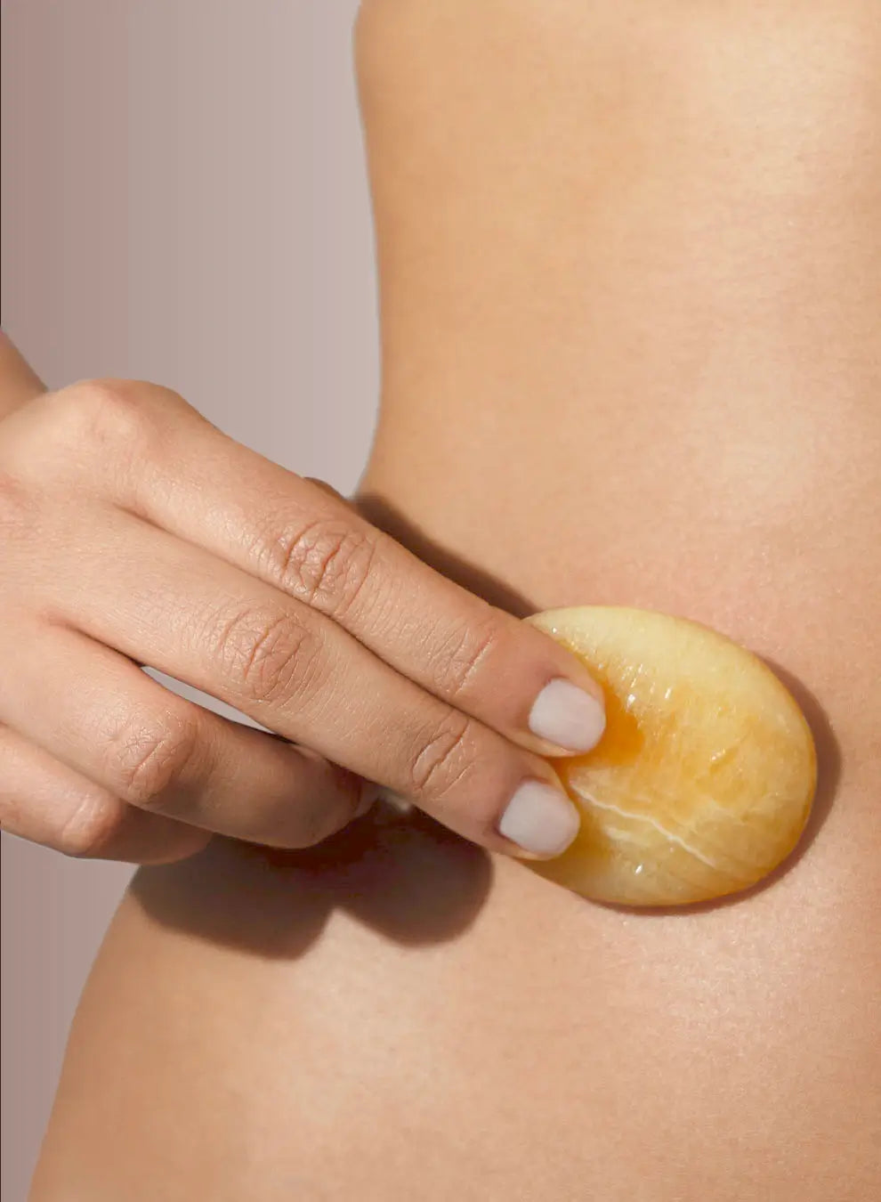 Hand holding a orange calcite stone to the abdomen on a neutral background