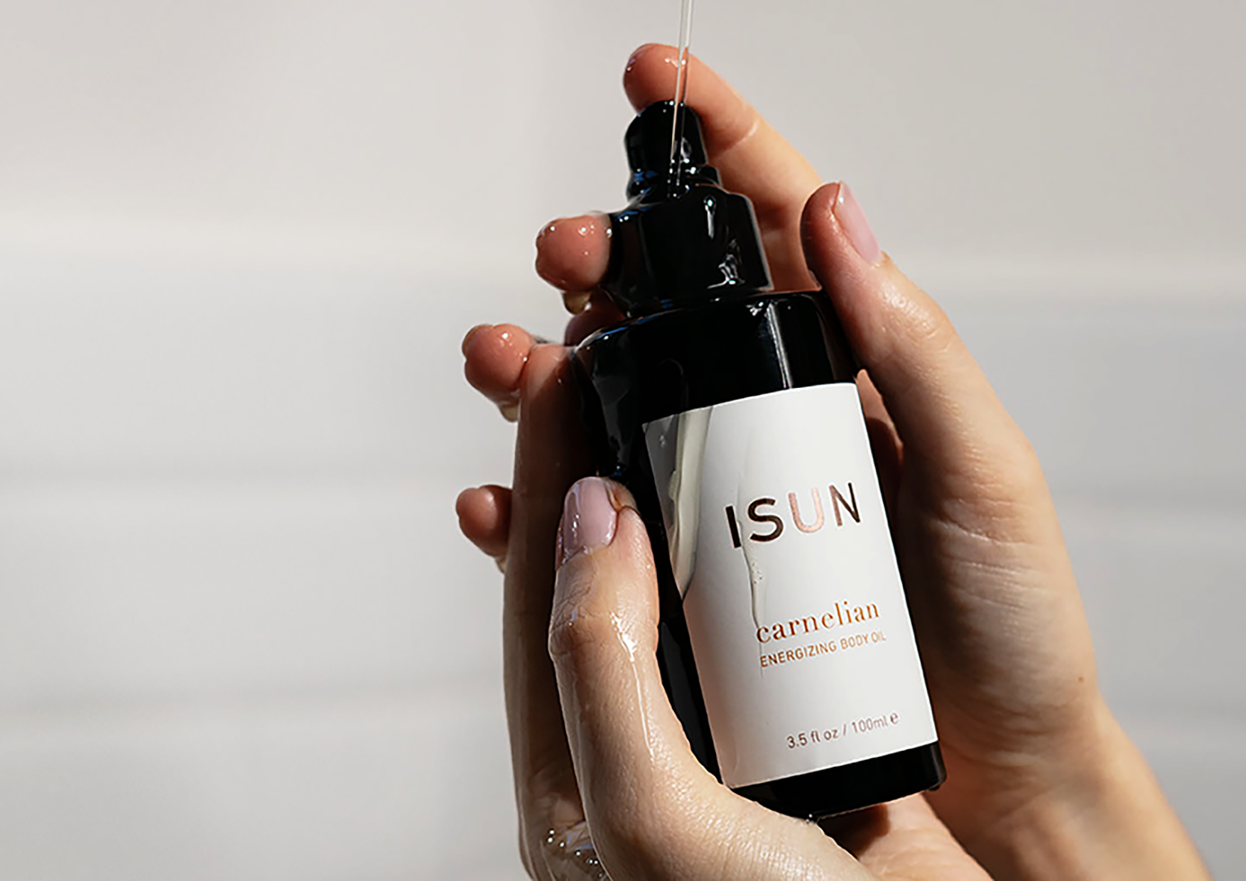 Hands holding a bottle of Carnelian body oil with oil dripping down 