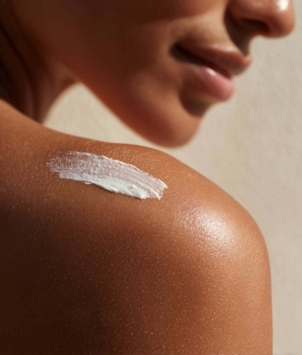 Close-up of a person's shoulder with a white cream application on a neutral background
