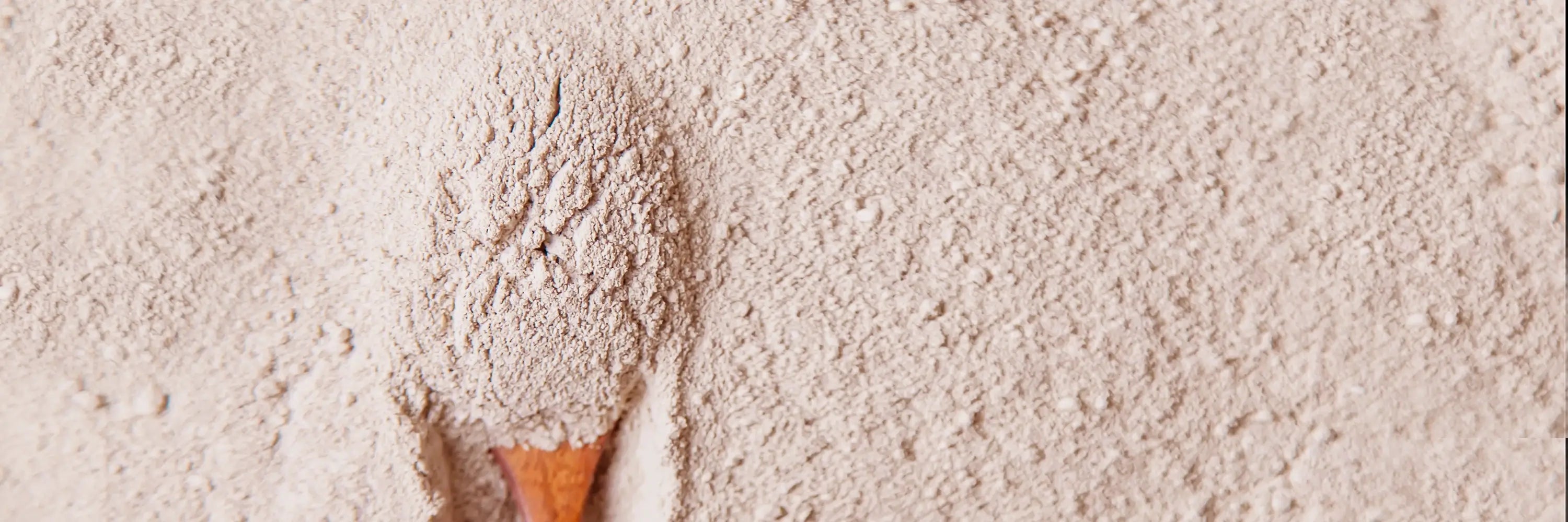 Wooden scoop filled with clay on a bed of Rhassoul clay
