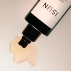 Cosmetic bottle with a pump dispensing oil on a neutral background