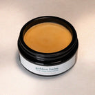 Jar of 'golden balm' face and body moisturizer on a neutral background