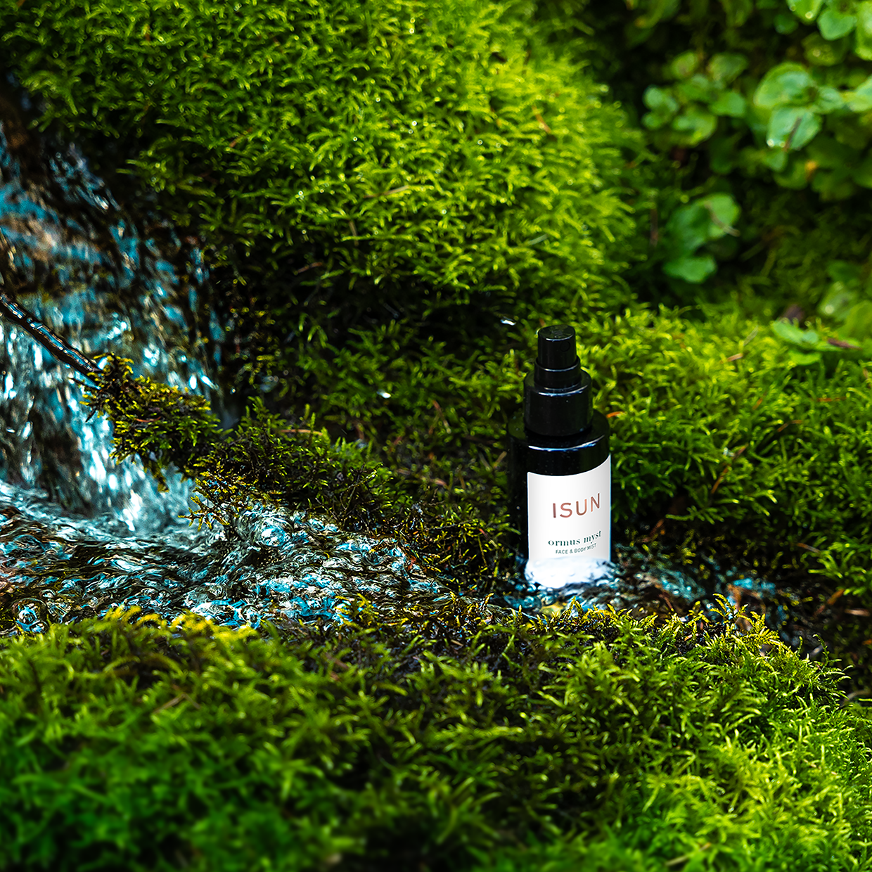 A bottle of ormus myst standing in a stream surrounded by moss