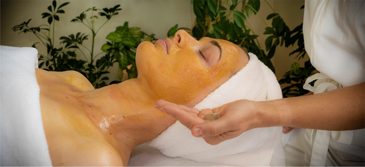Person receiving a facial treatment with a gold mask in a spa setting.