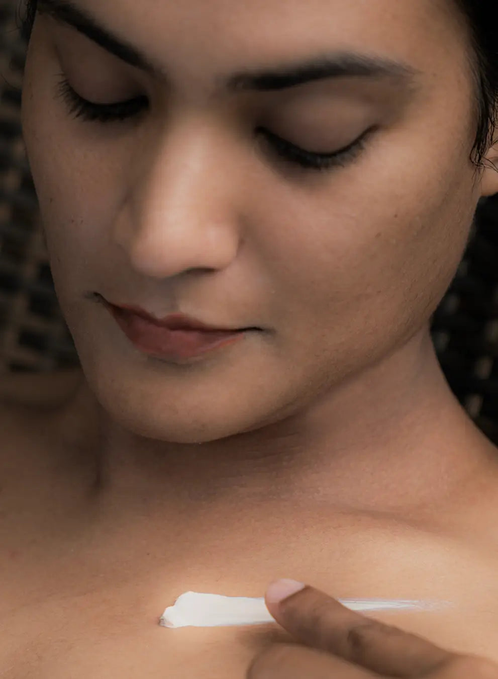 Person applying a white cream to their shoulder against a dark background