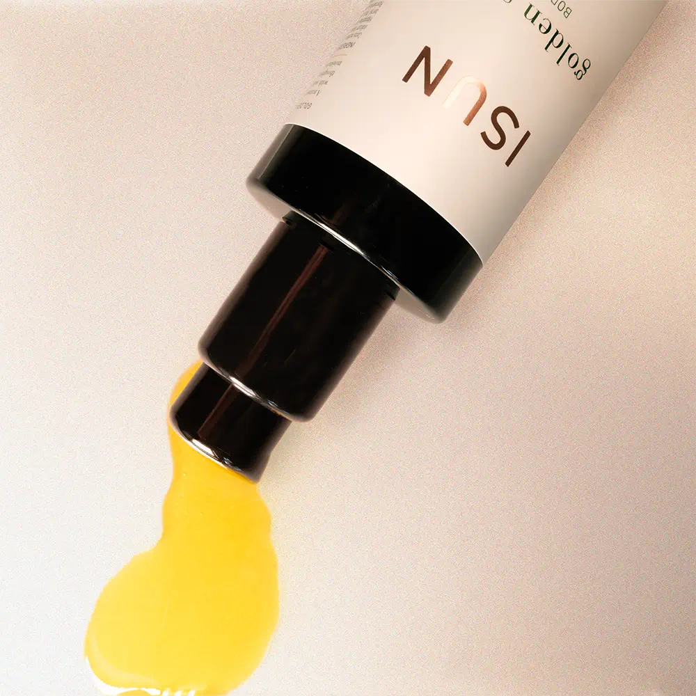Cosmetic product with yellow oil being squeezed out on a beige background