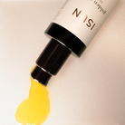 Cosmetic product with yellow oil being squeezed out on a beige background